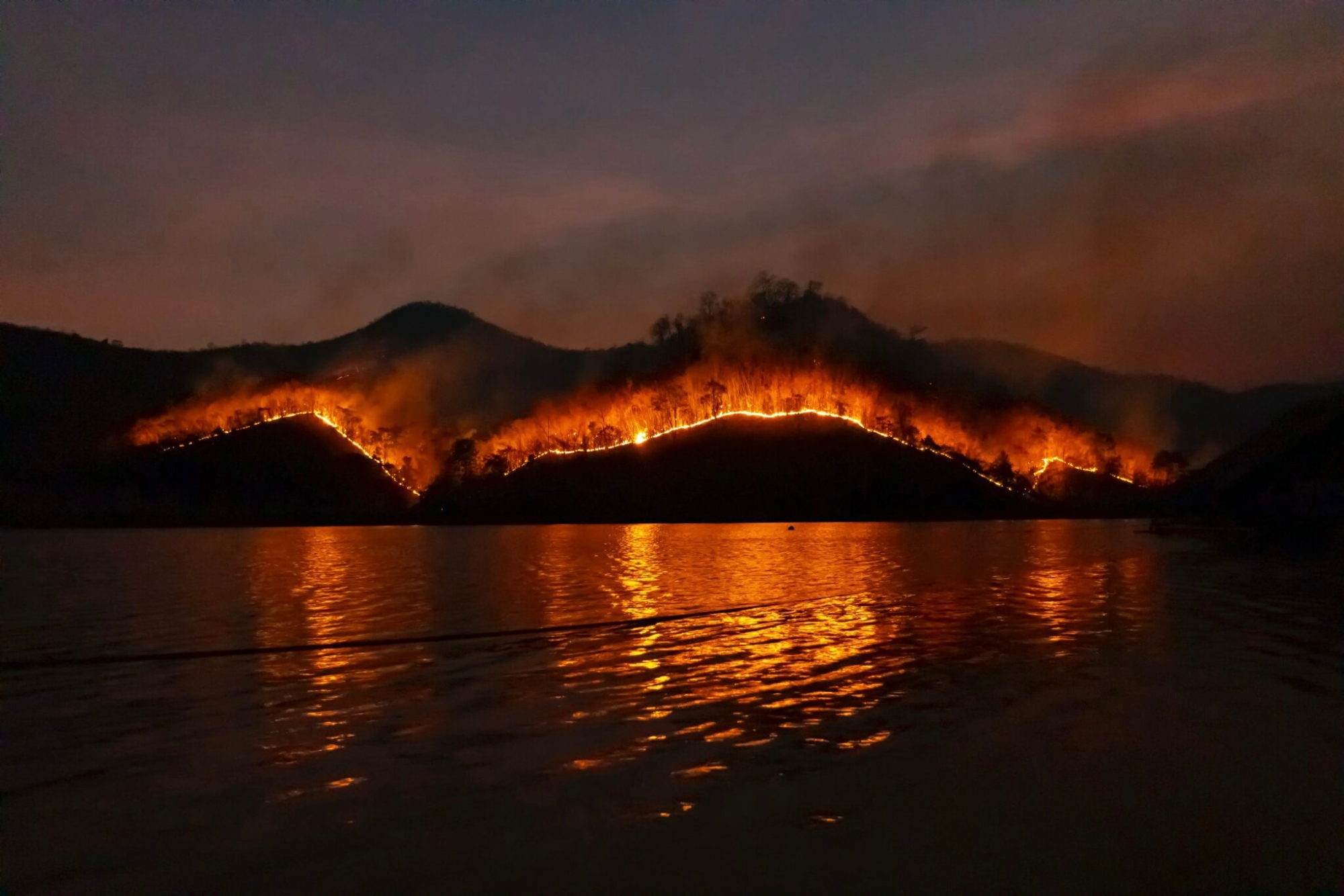 A photo of a fire burning on a hilltop at night